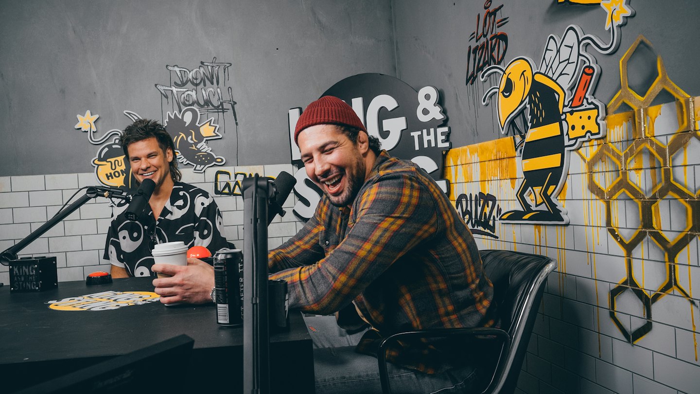 Two male podcasters laughing while recording in a studio.